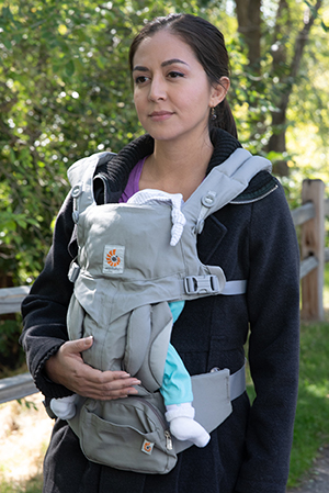 Mujer con un bebé en el portabebés frontal caminando al aire libre.