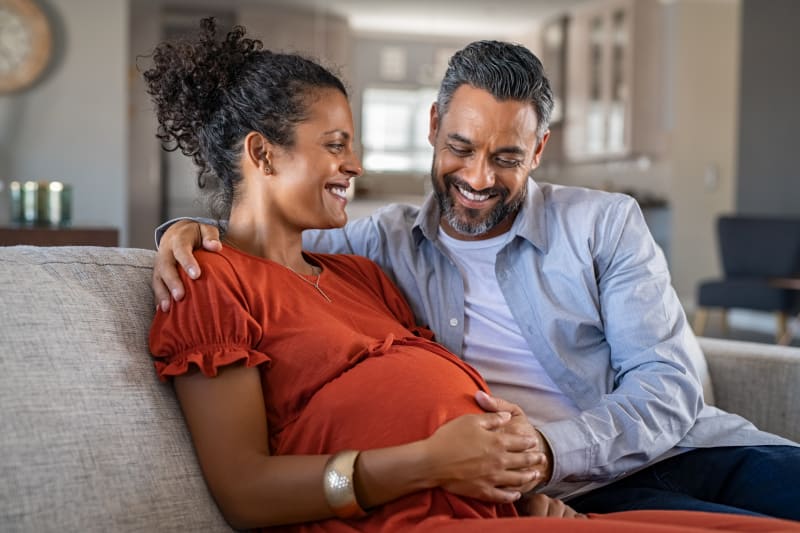 Pregnant couple sitting on couch at home.