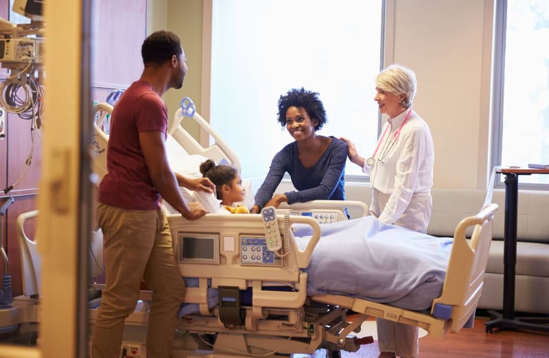 Parents speaking with doctor in daughter's hospital room.