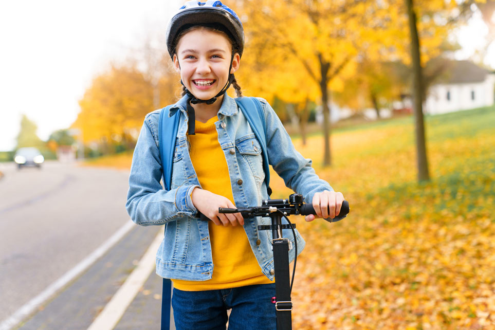 Smiling pre-teen girl wearing a helmet on a scooter.