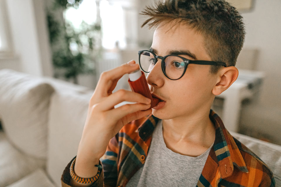 Teenage boy taking deep breath from his inhaler
