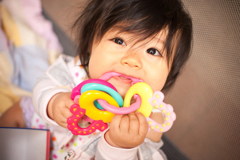 A baby girl with sore gums chews on a plastic teething ring.